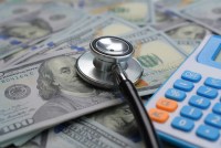 A photo of a stethoscope and calculator next to a pile of money.