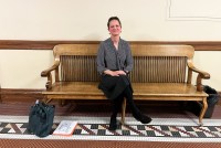 A photo of a woman sitting for a portrait on a bench indoors.