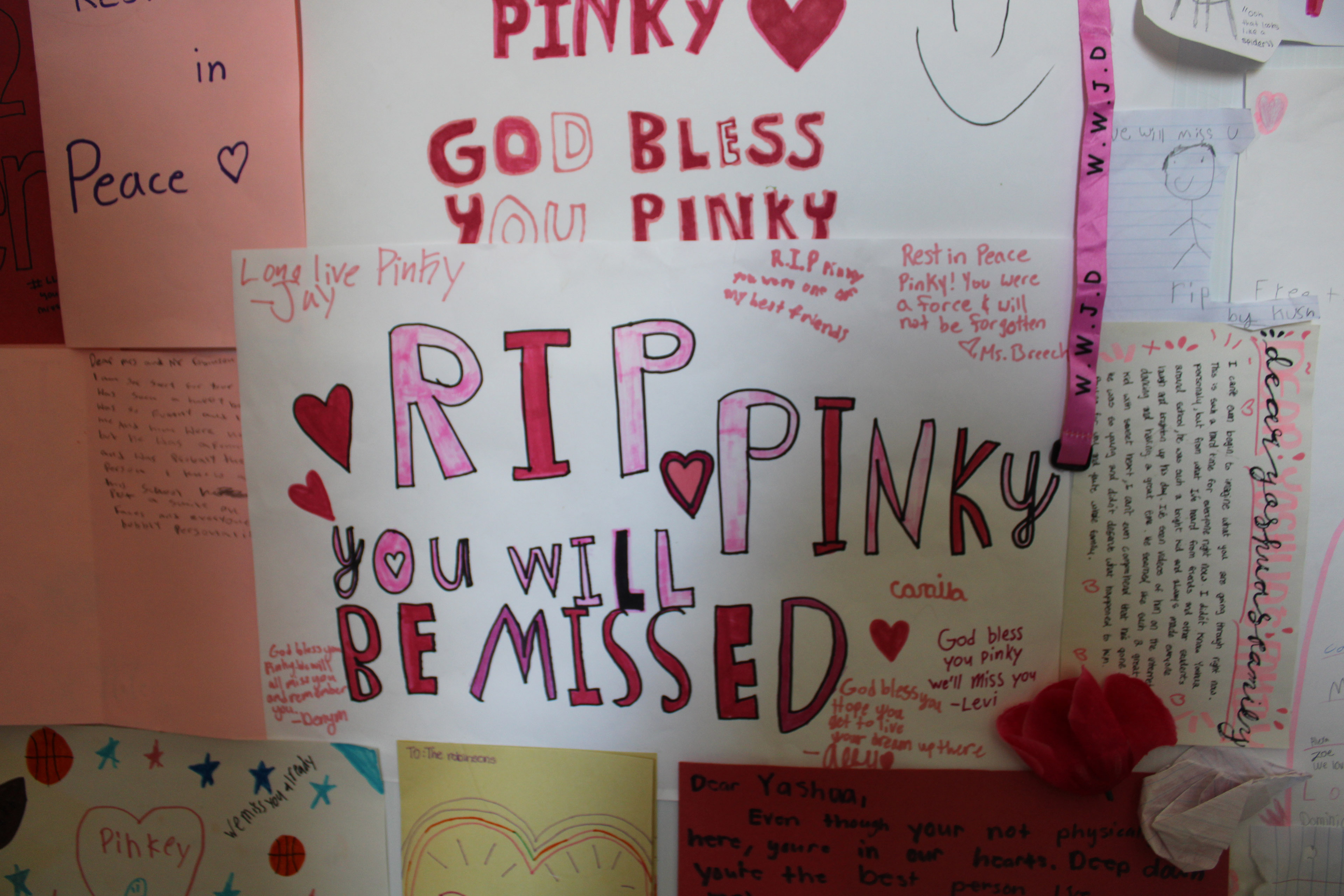 An up-close photo of memorial cards for Yahushua Robinson. The card in the center reads, "RIP Pinky, you will be missed."